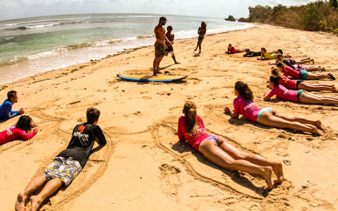 Surf instructor teaching a group on a Bali beach, practicing on sand before hitting the waves.
