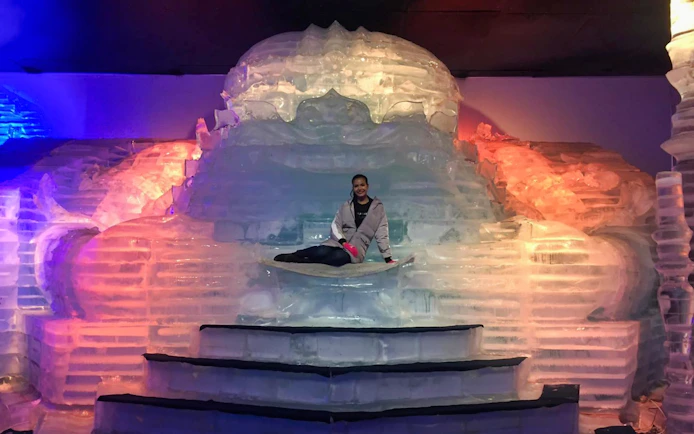 Person sitting on an ice sculpture at Frost Magical Ice of Siam, illuminated by colorful lights.