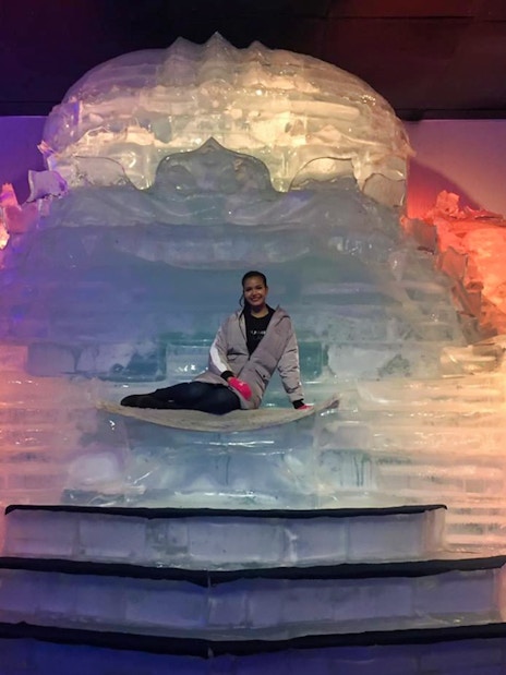 Person sitting on an ice sculpture at Frost Magical Ice of Siam, illuminated by colorful lights.