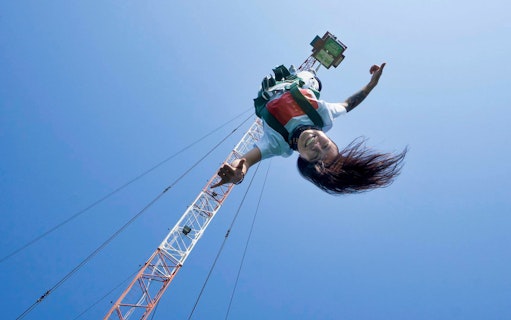 Person bungy jumping from a tall crane against a clear blue sky.