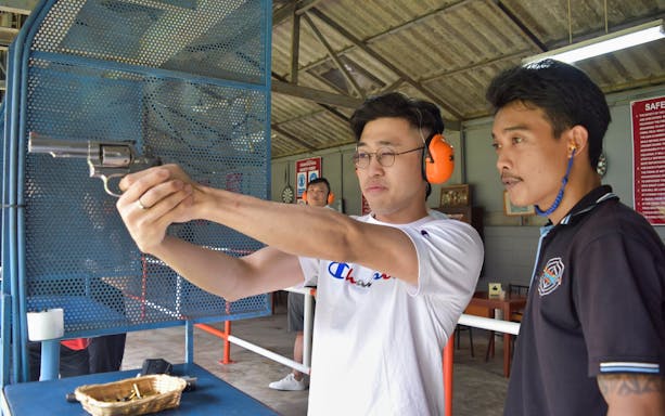 Man aiming .22 caliber revolver with instructor at Pattaya Shooting Park.
