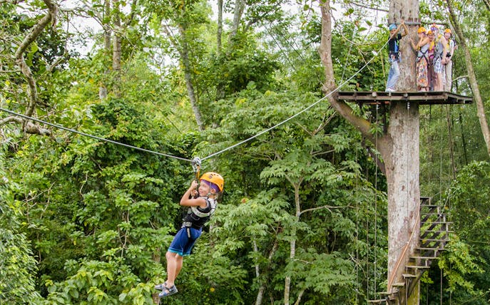 Child ziplining through lush forest at Flight Of The Gibbon Chonburi, Thailand.