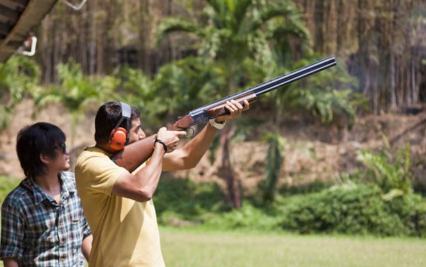 Man aiming shotgun at Pattaya Shooting Park with instructor nearby.