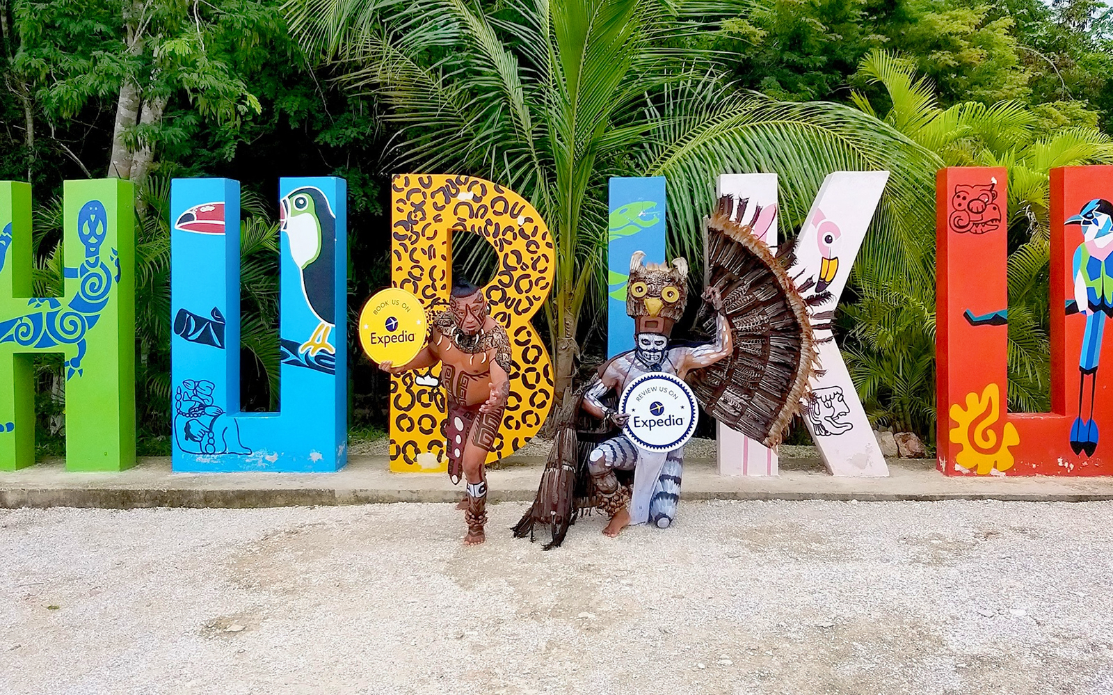 Colorful Hubiku sign with two performers in traditional costumes, Chichén Itzá tour.