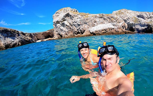 Snorkelers in clear blue water near rocky cliffs at Marietas Islands, Mexico.