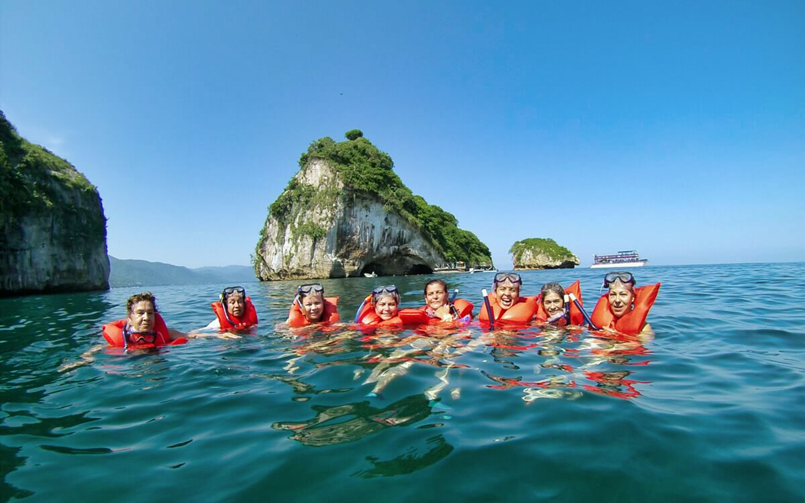 Snorkelers in life vests at The Arches, Puerto Vallarta, with rocky islets in the background.