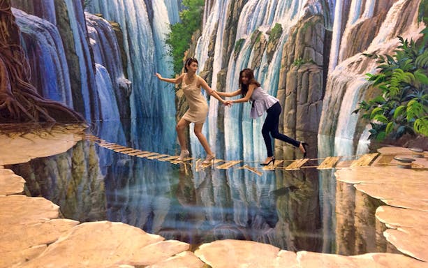 Two people balancing on a 3D art bridge over water at Art in Paradise Chiang Mai.