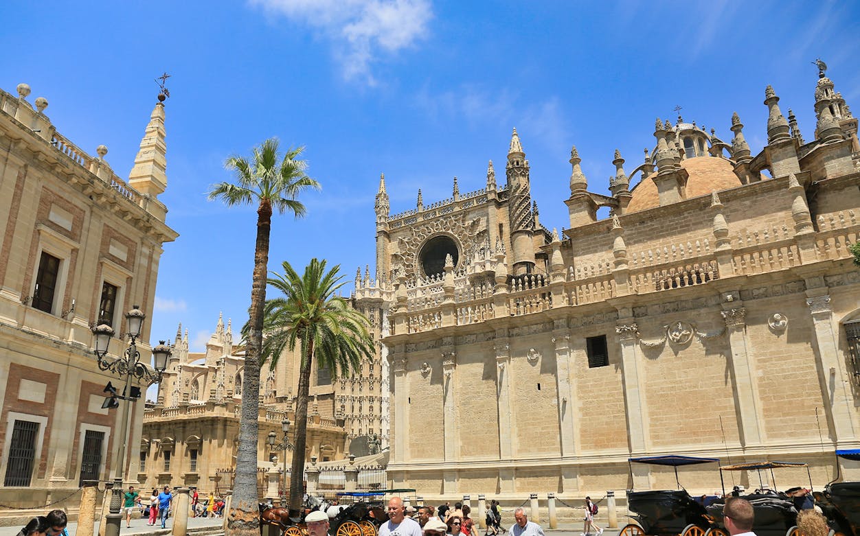 Seville Cathedral exterior with tourists and horse-drawn carriages in Seville, Spain.