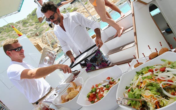 Guests enjoying lunch on a catamaran sailing tour with salads and sandwiches.