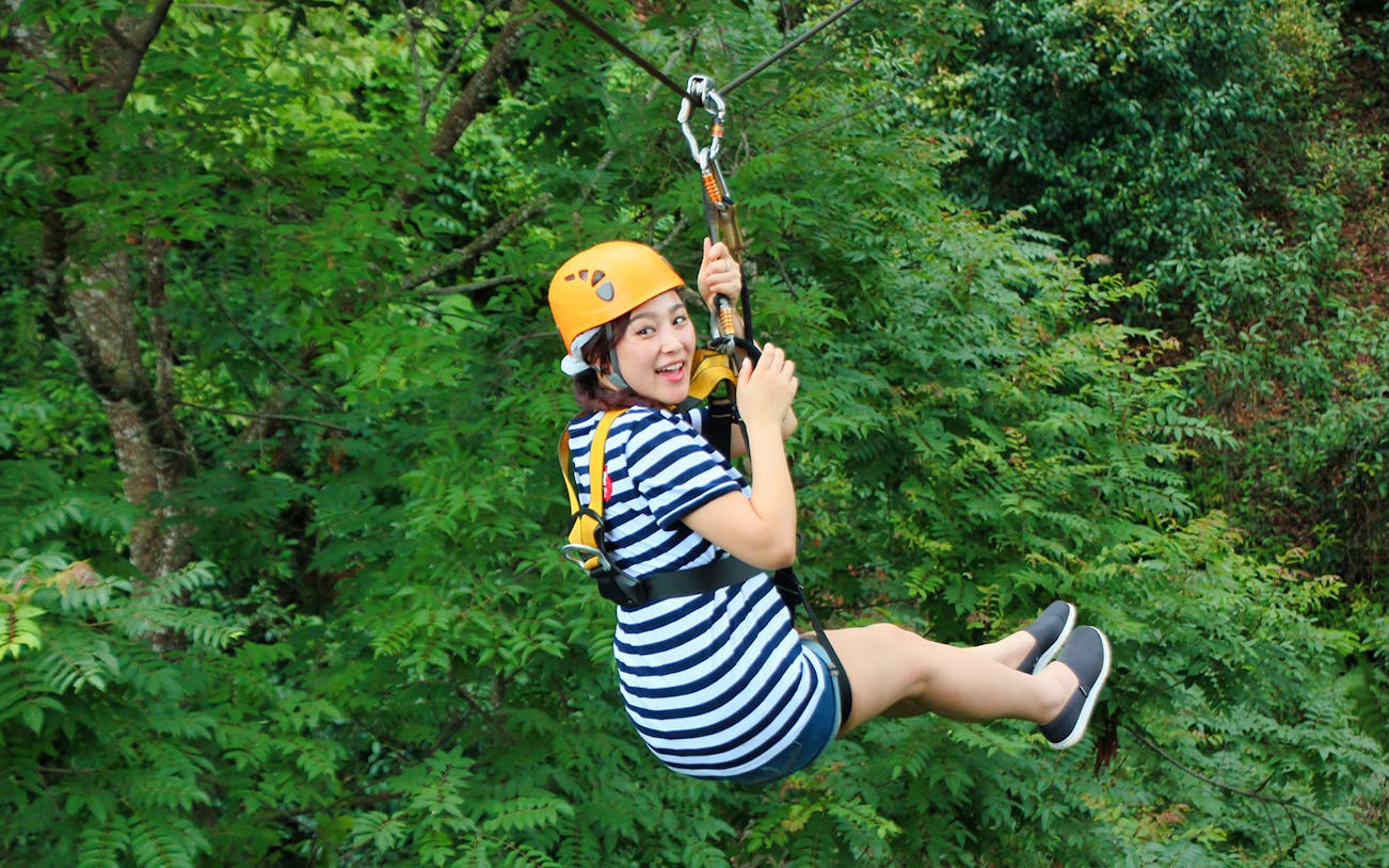 Person ziplining through lush jungle canopy on Jungle Flight Zipline Adventure.