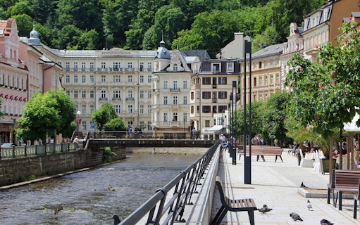 Karlovy Vary riverside promenade with historic buildings and lush greenery.