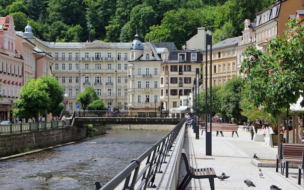 Karlovy Vary riverside promenade with historic buildings and lush greenery.