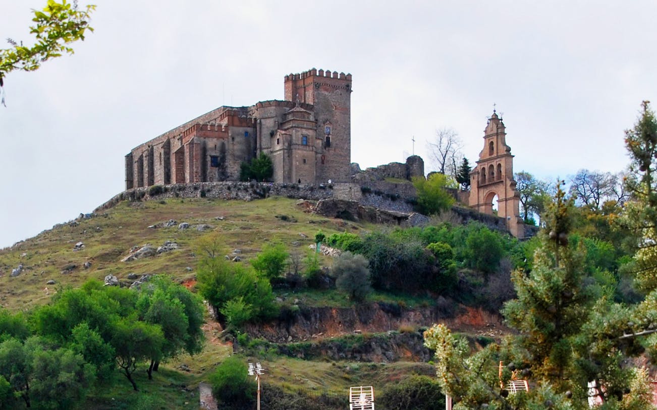 Aracena Castle on a hilltop surrounded by greenery, part of Aracena & Riotinto Day Trip from Seville.