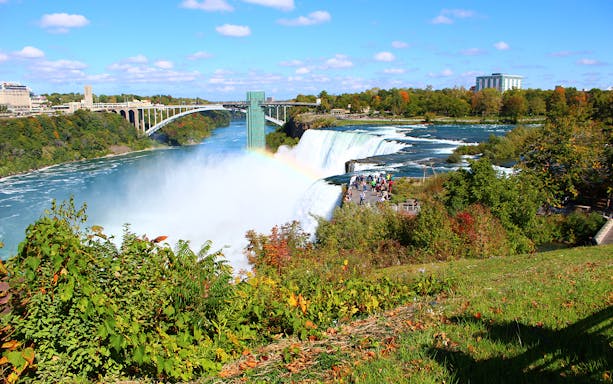 Niagara Falls with rainbow and tourists at Cave of the Winds viewing platform.