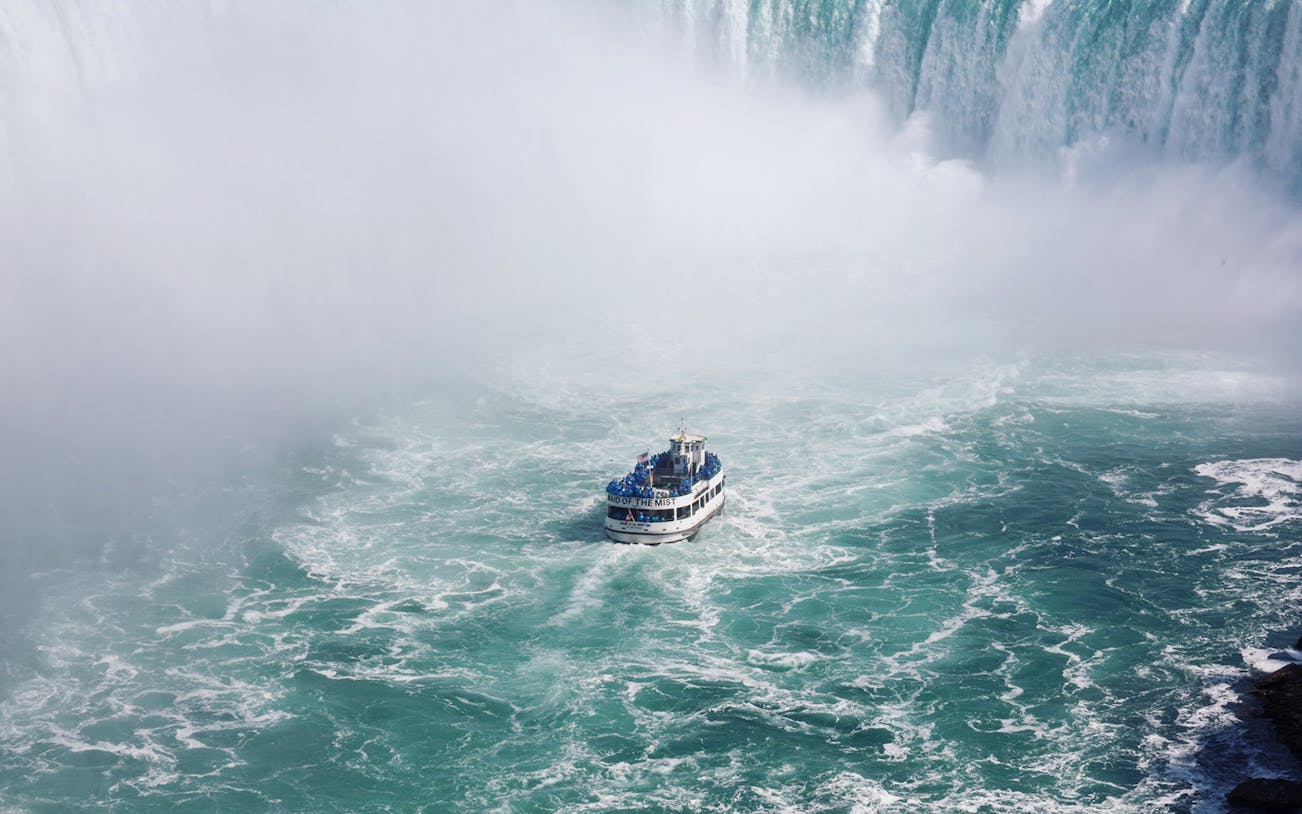 Maid of the Mist boat approaching Niagara Falls surrounded by mist and cascading water.