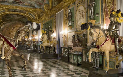 Knights in armor on horseback in the Royal Palace of Turin's ornate hall.