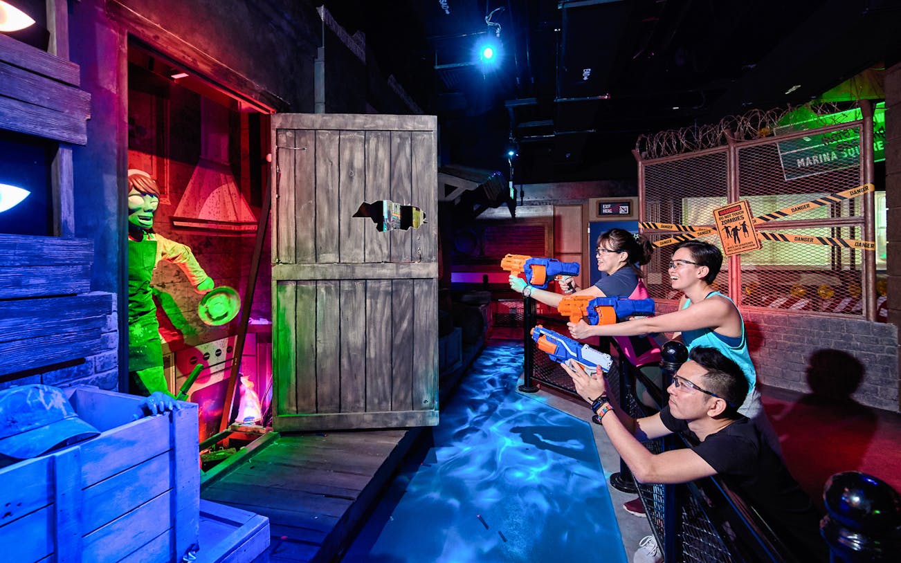 Visitors aiming NERF blasters at a zombie target in a themed arena at NERF Action Xperience.