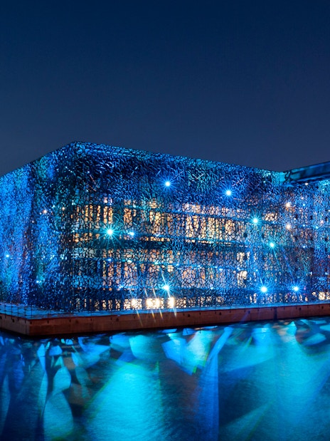 Mucem in Marseille illuminated at night, reflecting on the water.
