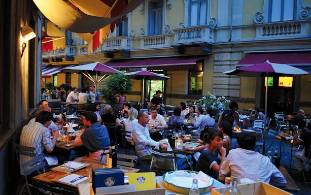 Outdoor dining at a bustling café in Torino, Italy, under colorful umbrellas.