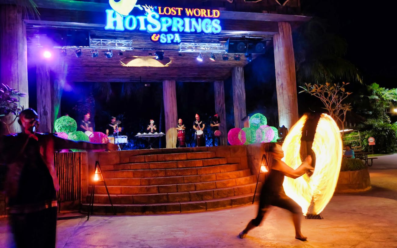 Fire performer at Lost World Hot Springs Night Park with live band on stage.