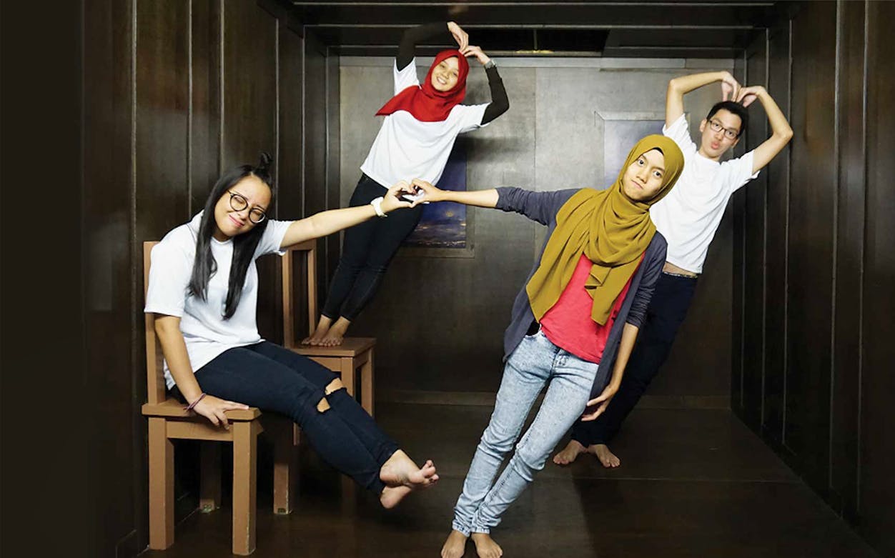 Visitors posing in a tilted room at Penang 3D Trick Art Museum.