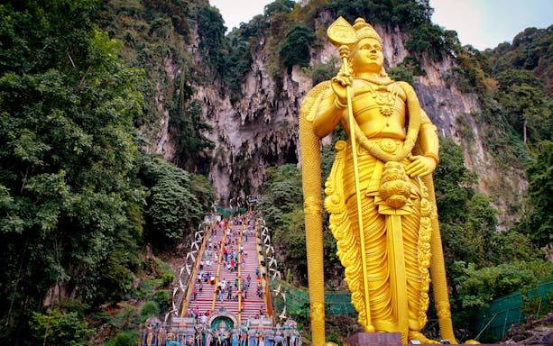 Batu Caves entrance with golden Murugan statue and colorful steps, Malaysia.