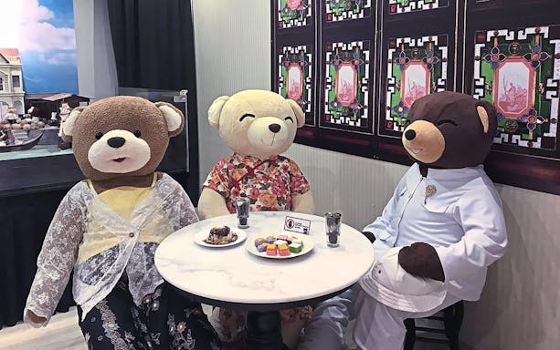 Teddy bears in traditional attire seated at a table in Penang TeddyVille Museum.