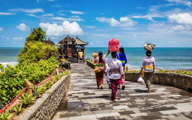 Visitors walking towards Tanah Lot Temple along a coastal path in Bali, Indonesia.