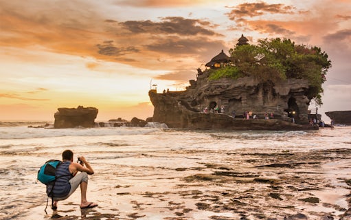 Tourist photographing Tanah Lot Temple at sunset, Bali, during a guided tour.