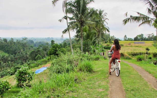 Cyclist on a path through lush greenery near Tanah Lot Temple, Bali.