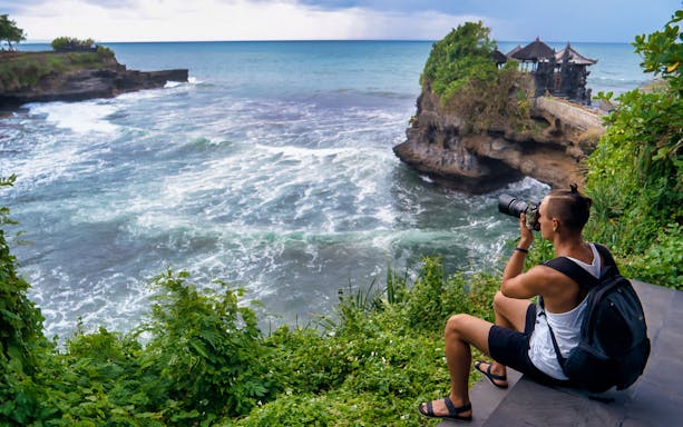 Photographer capturing Tanah Lot Temple on Bali's coast during guided tour.