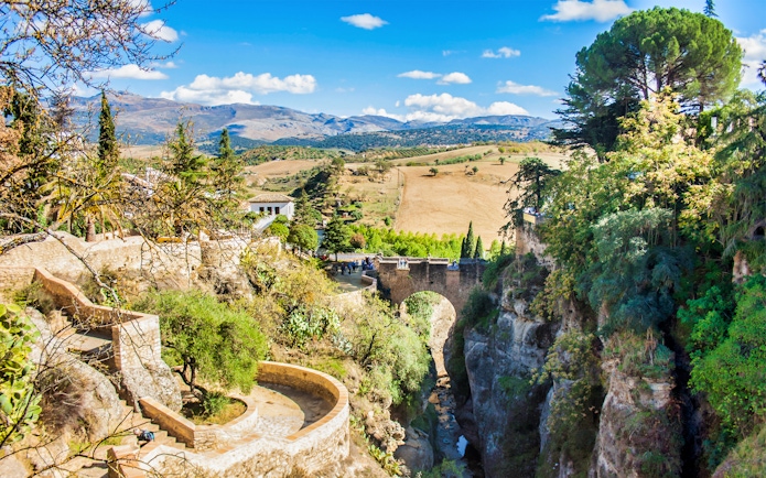 Ronda's Puente Nuevo bridge spanning a deep gorge, surrounded by lush greenery and distant hills.