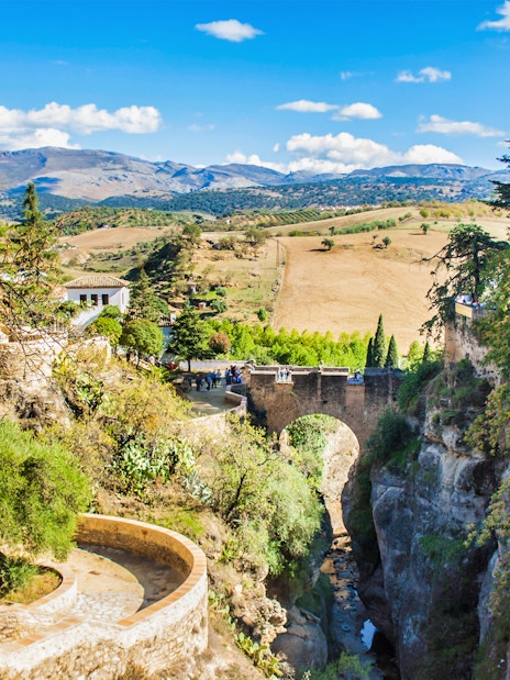 Ronda's Puente Nuevo bridge spanning a deep gorge, surrounded by lush greenery and distant hills.