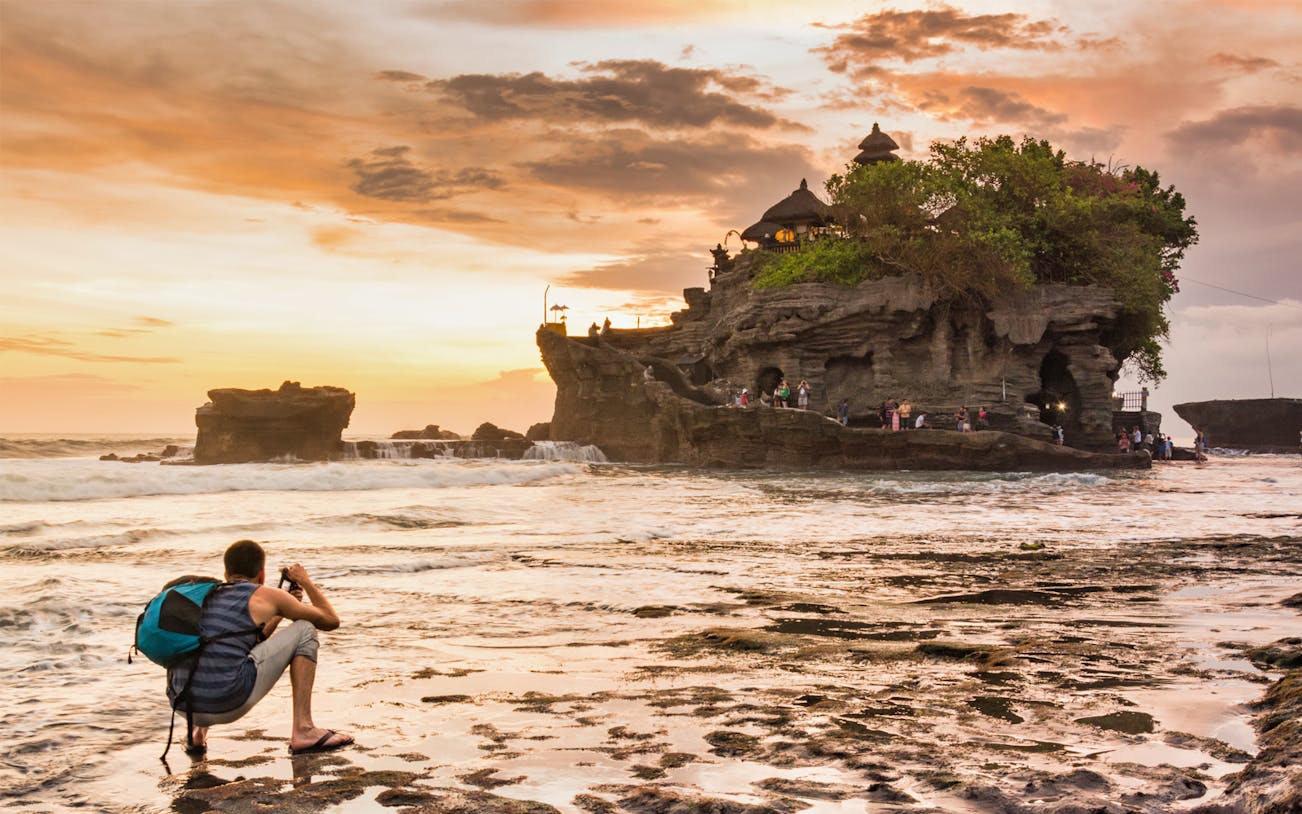 Tanah Lot Temple at sunset with tourists on a small group tour, Bali.