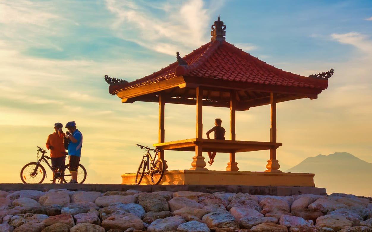 Cyclists at Sanur Beach gazebo during sunrise, Bali bike tour.