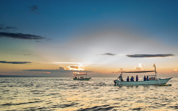 Boats with tourists watching dolphins at sunrise on Lovina Beach, Bali.