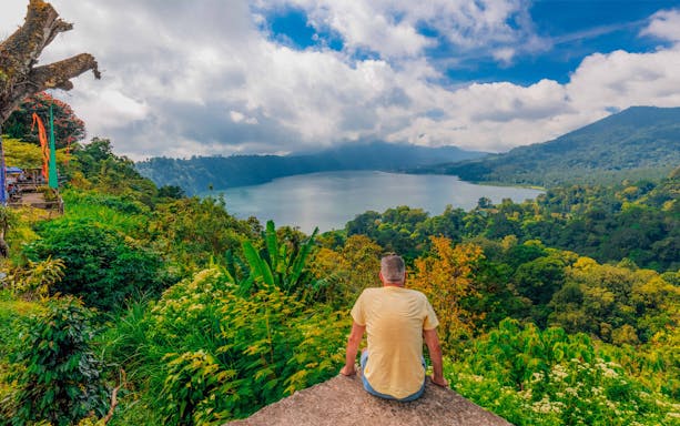 Person overlooking lush landscape and lake in Bali during trekking tour.