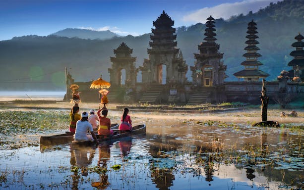 People in a canoe on a lake near Handara Gate, Bali, with misty mountains in the background.