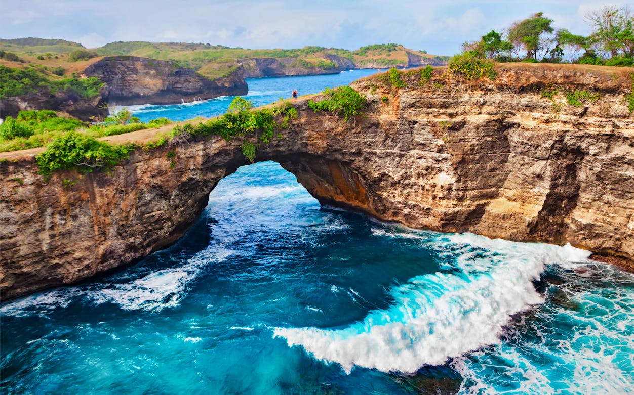 Natural rock arch over blue ocean waves at West Nusa Penida, Indonesia.