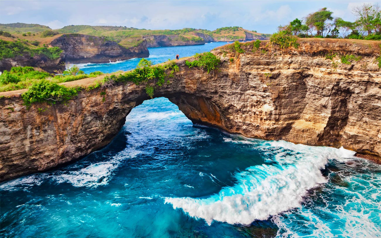 Natural rock arch over blue ocean waves at West Nusa Penida, Indonesia.