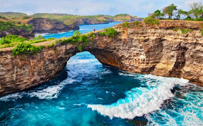 Natural rock arch over blue ocean waves at West Nusa Penida, Indonesia.