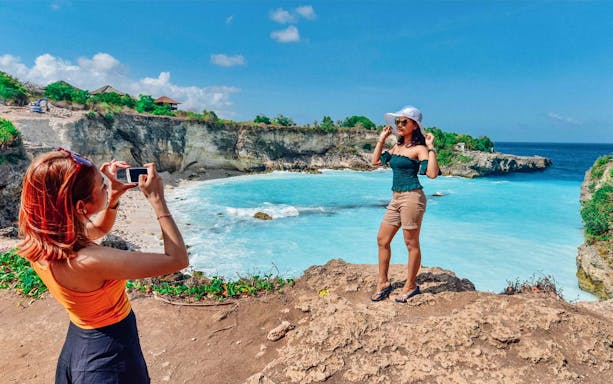 Tourists at Blue Lagoon, Bali, with clear blue water and rocky cliffs in the background.