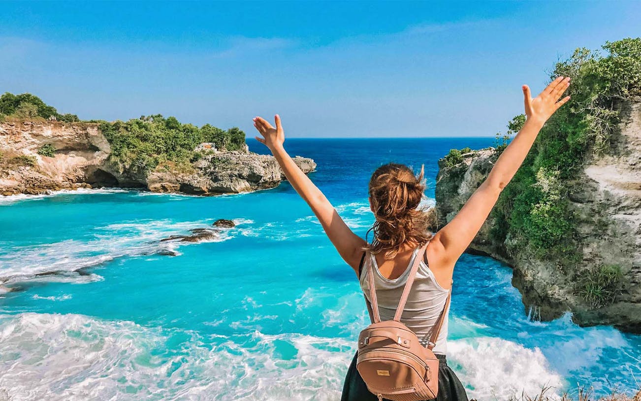 Person enjoying view of Blue Lagoon, Bali, with clear turquoise water and rocky cliffs.