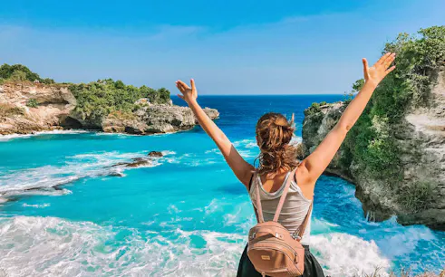Person enjoying view of Blue Lagoon, Bali, with clear turquoise water and rocky cliffs.