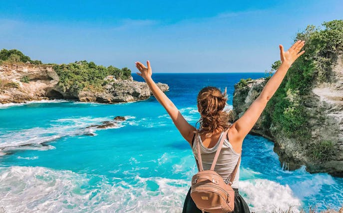 Person enjoying view of Blue Lagoon, Bali, with clear turquoise water and rocky cliffs.