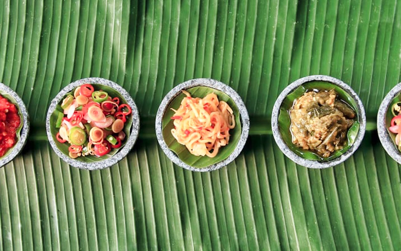 Bowls of Balinese ingredients on banana leaves for a cooking class.