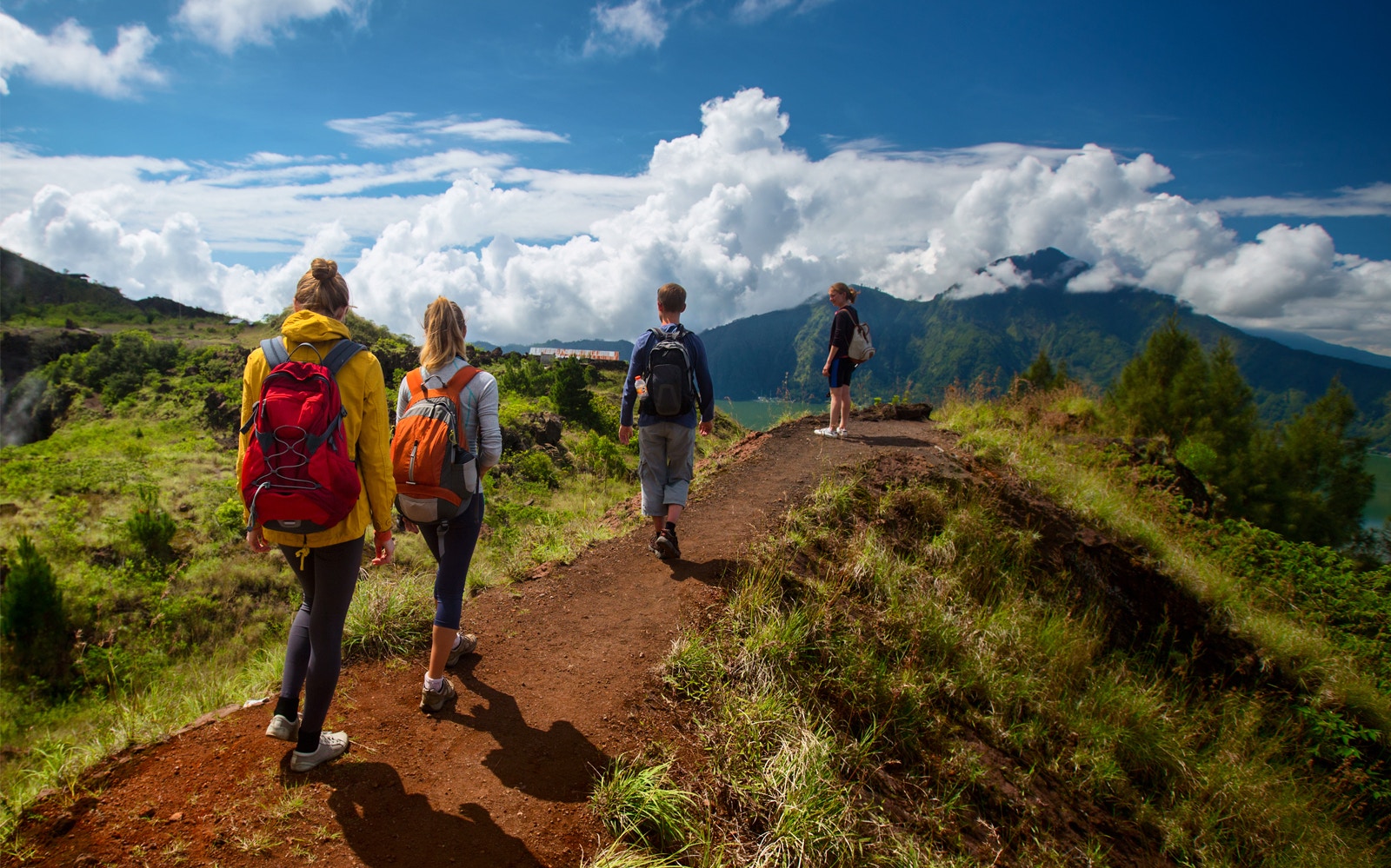 Hikers on Mount Batur trail with scenic view of mountains and clouds in Bali.
