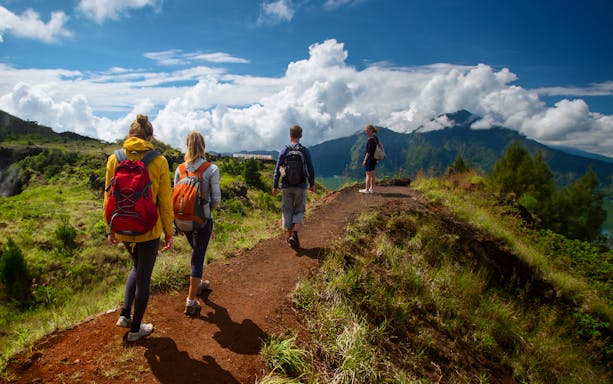 Hikers on Mount Batur trail with scenic view of mountains and clouds in Bali.