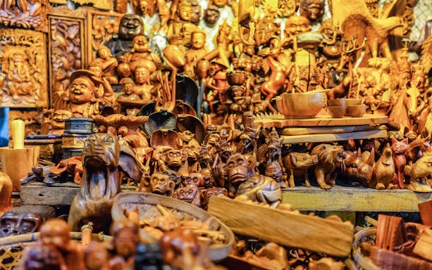Wooden carvings at a traditional market in Denpasar, Bali, featuring various animal and human figures.