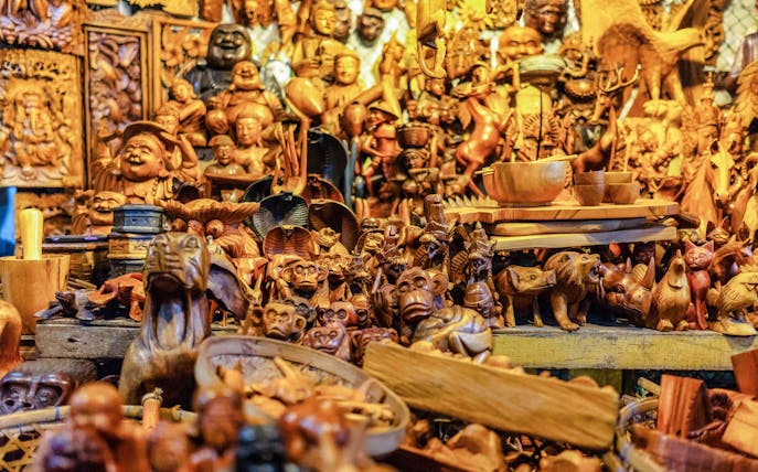 Wooden carvings at a traditional market in Denpasar, Bali, featuring various animal and human figures.